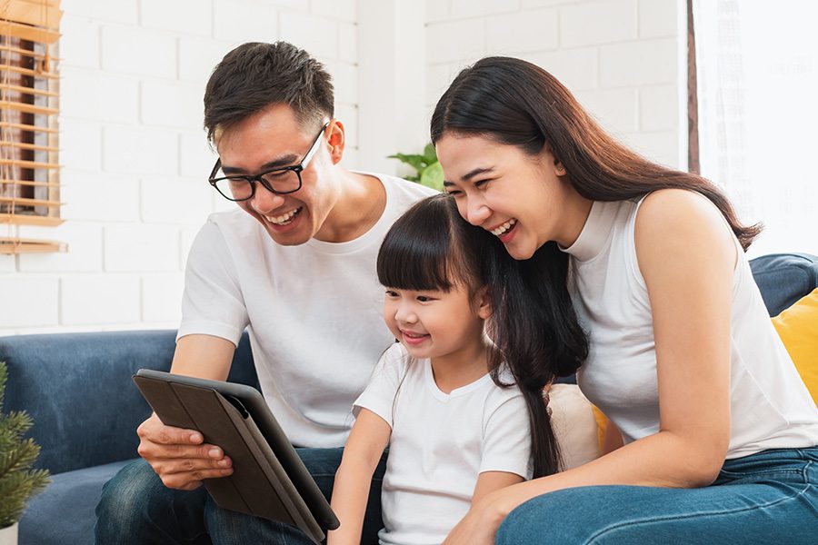 Client Center - Happy Family Spending Time Together Sitting on a Sofa at Home Using a Tablet